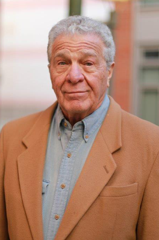 A man in a brown jacket and blue shirt.