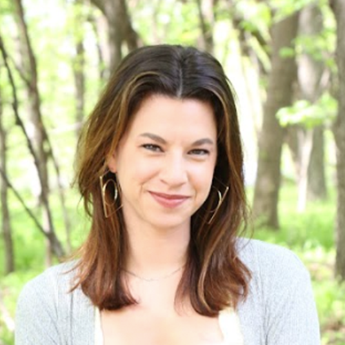 A woman with long hair standing in the woods.